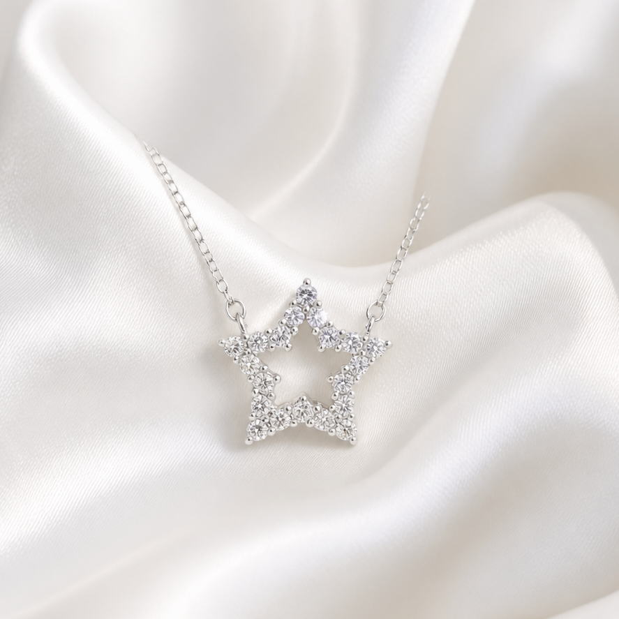 A silver star-shaped pendant necklace adorned with small clear stones, displayed on draped white satin fabric.