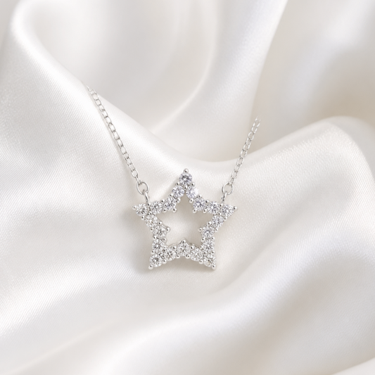A silver star-shaped pendant necklace adorned with small clear stones, displayed on draped white satin fabric.