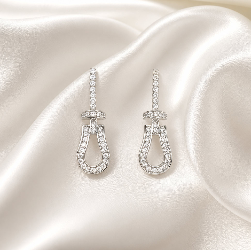 A pair of silver-tone drop earrings with clear gemstones, displayed on draped cream satin fabric.